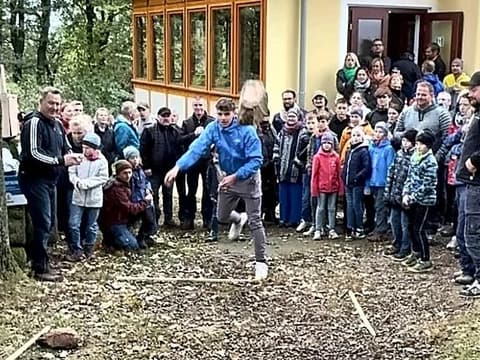 Granitstein-Wettkampf: Ein Werfer holt mit dem Stein aus, die Zuschauer stehen im Halbkreis vor der Baude